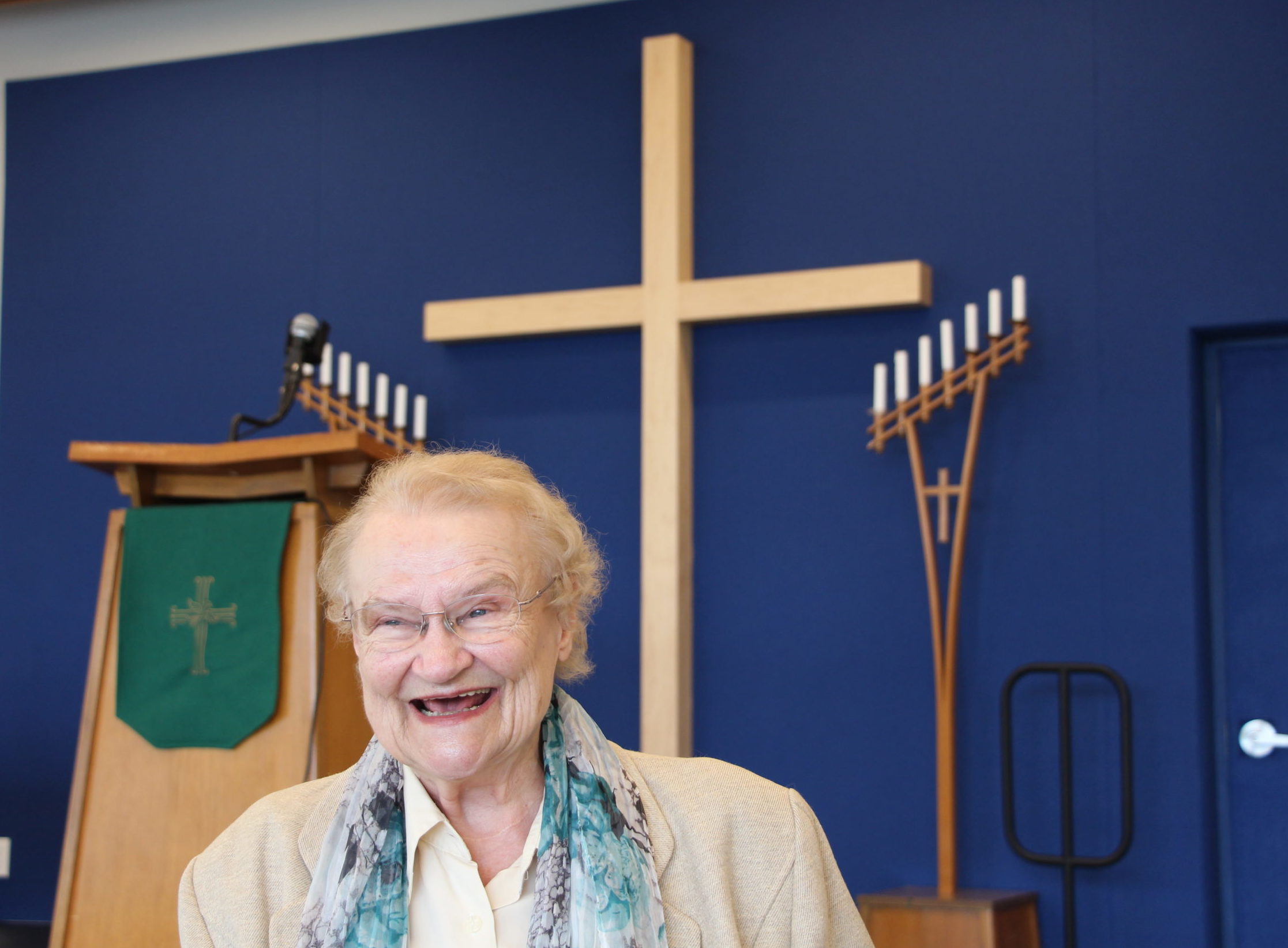 Hannelore Gerlach stands at the front of Oakridge Lutheran Church, a wooden cross behind her