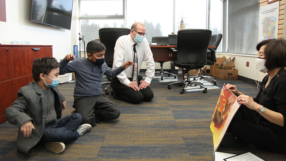 Jordan Tinney sits with two students on the ground as they listen to a story.