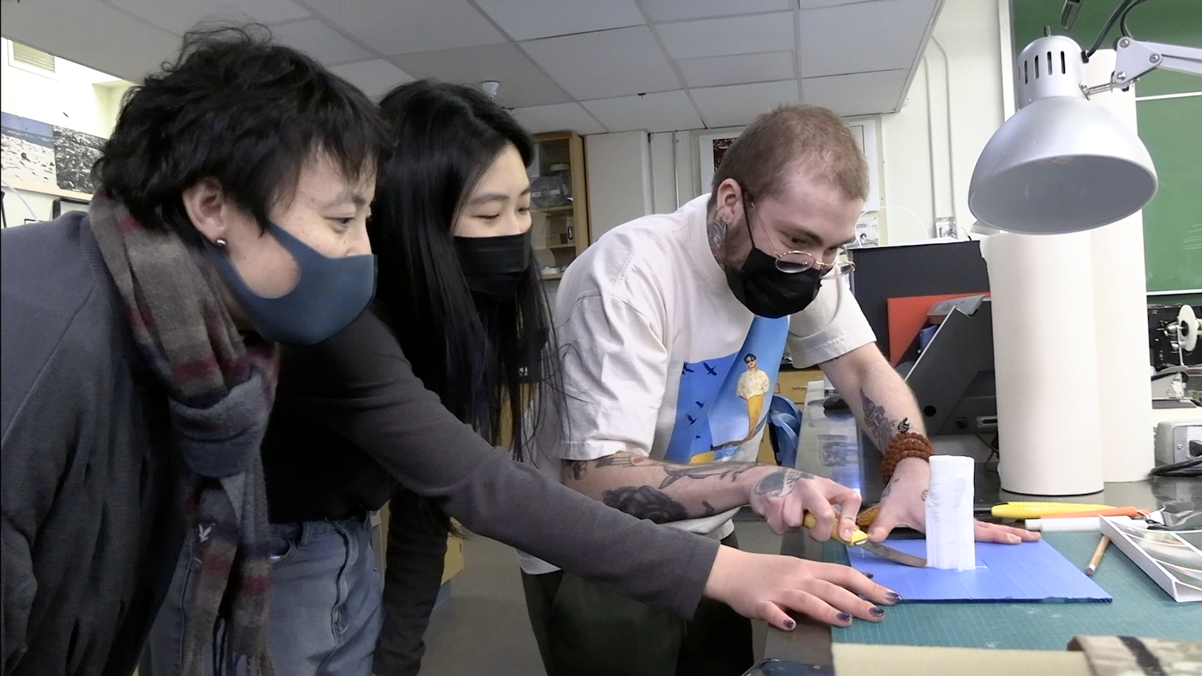 Three students work on a freshly printed 3D model of an ancient Chinese mask.