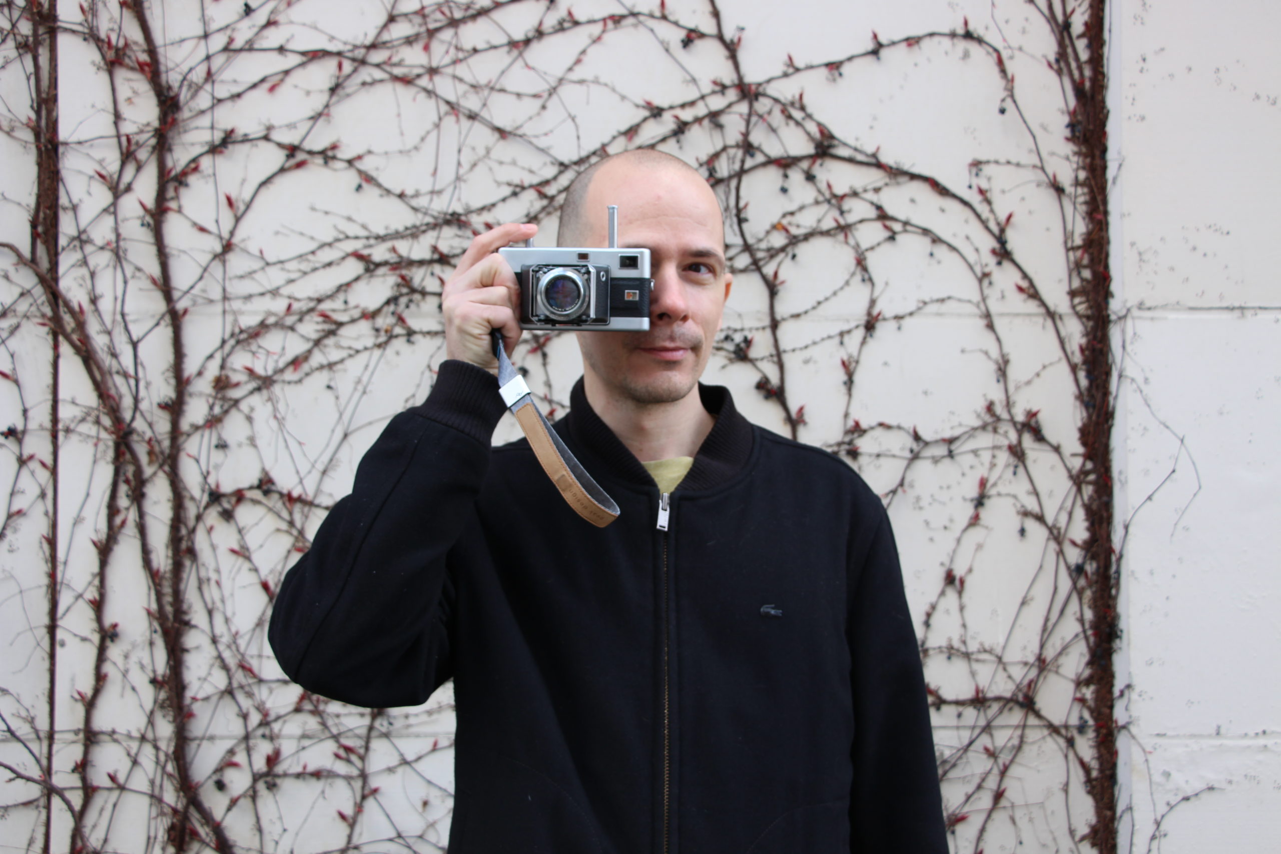 A man stands with an analogue film camera up to his face, his finger rests on the shutter button.
