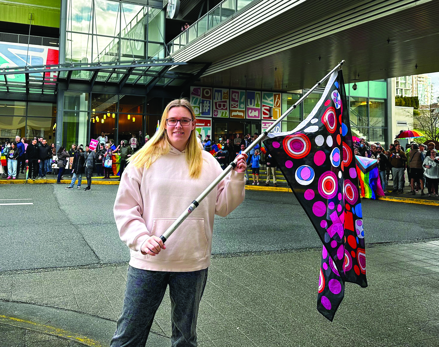 Nicola Spurling outside Coquitlam public library holding colourful flag
