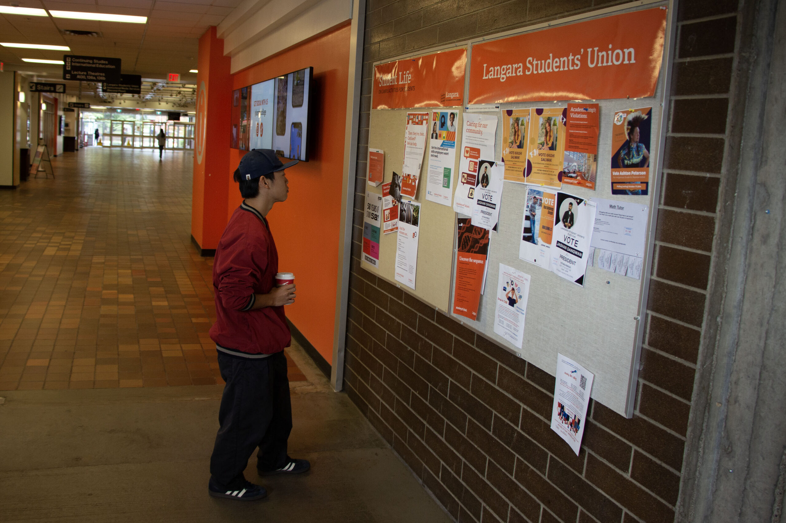 A student looks at the Langara Students' Union bulletin board with various flyers pinned.