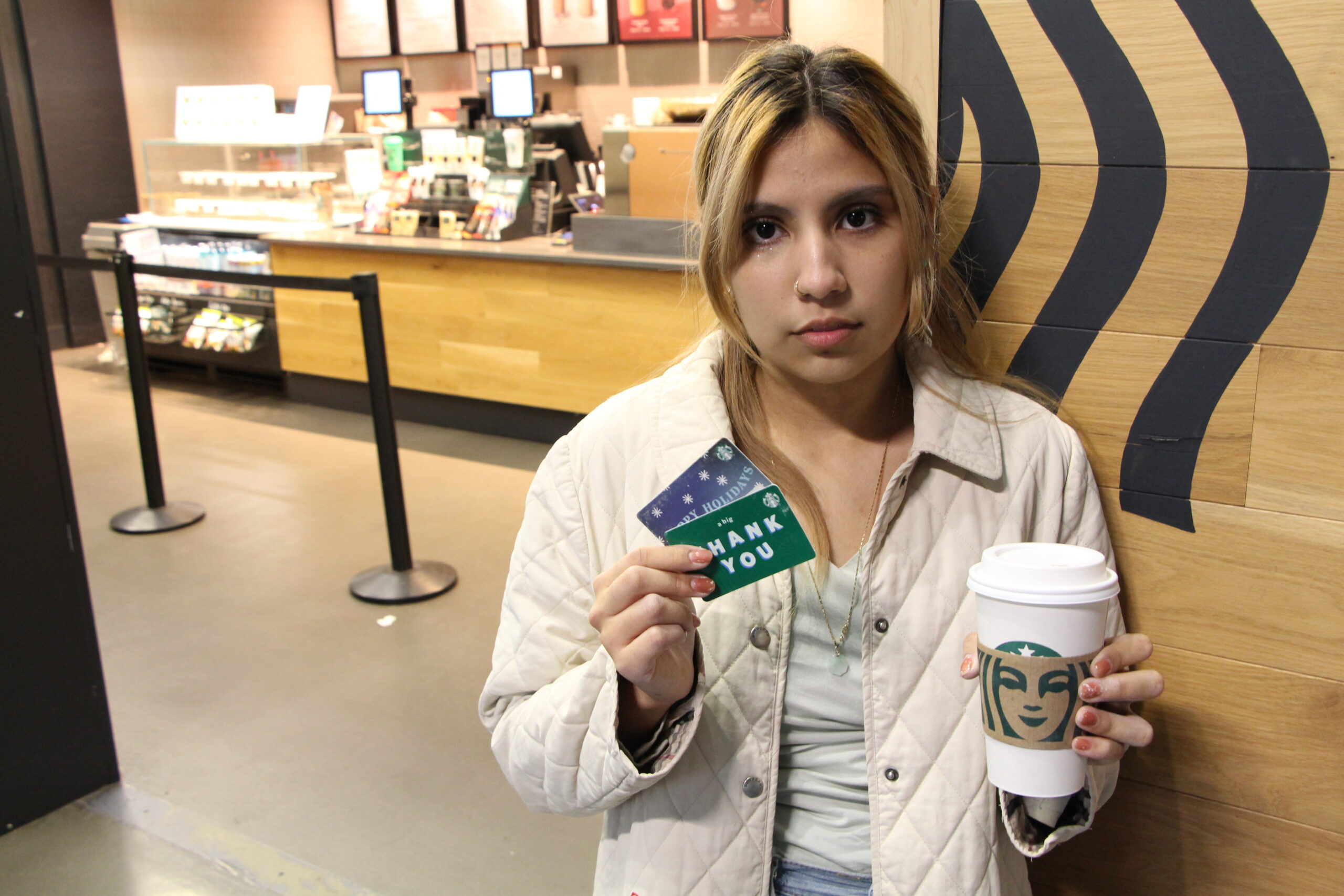 Naomi Damian stands in front of the campus Starbucks with gift cards in one hand and a Starbucks cup in the other.