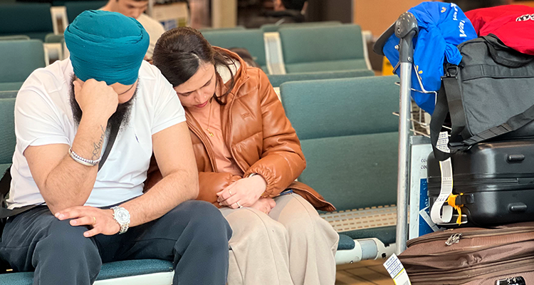 An exhausted looking couple sit and wait for their flight in an airport lounge