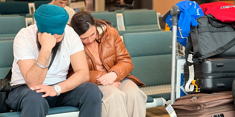 An exhausted looking couple sit and wait for their flight in an airport lounge
